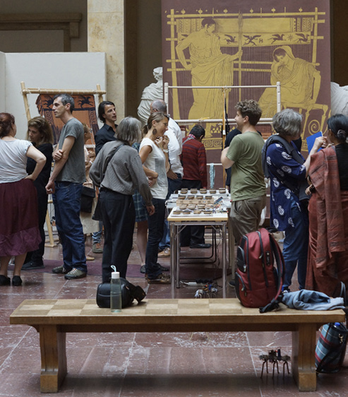 A group of people engages in lively conversation at an exhibit of ancient looms and sculptures.