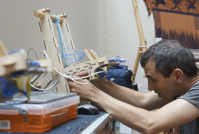 A person focussed on preparing a small loom model within a workshop setting.