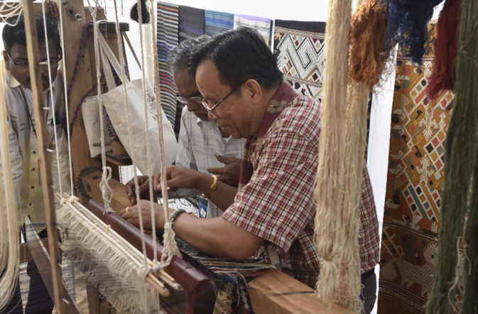 Two weavers work on a traditional loom.