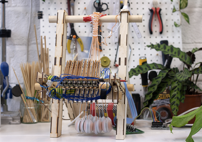 Small model of a warp-weighted loom with an electronic mechanism for selecting warp threads.