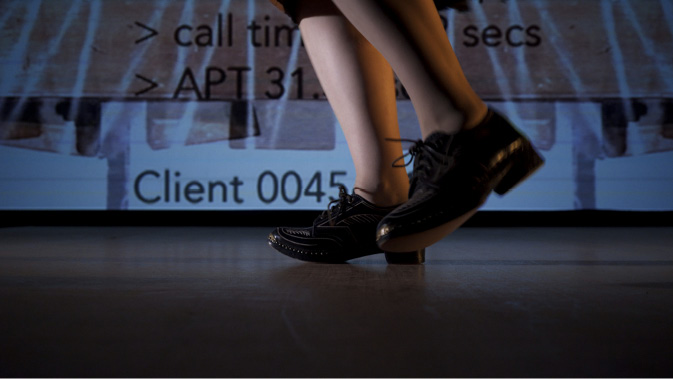 Video still of a person clog dancing against a backdrop of projected text.