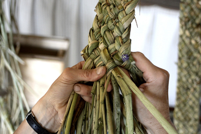 Hands weaving bulrush strands into a tight braid, showcasing intricate craftwork.