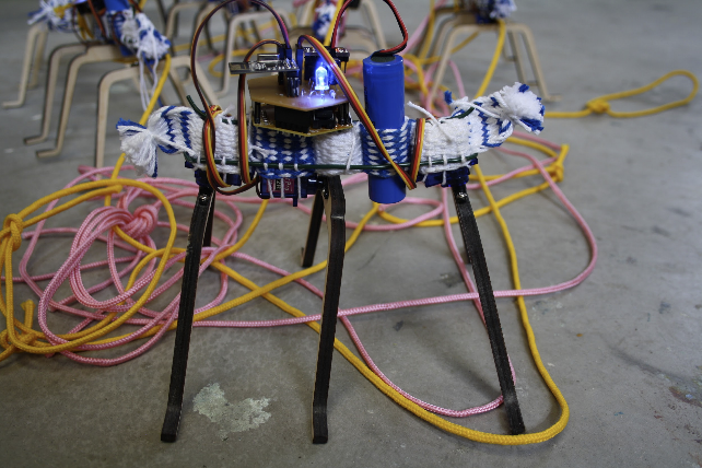 Small, ant-like robot made from textile braid, wood and wire carrying small electronic elements.