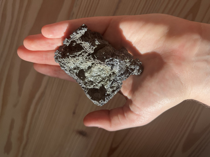 Outstretched hand holding large dark lava stone.