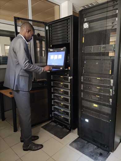 A man in a grey suit looks at a laptop in front of a tall black metal box that contains the ID card server.