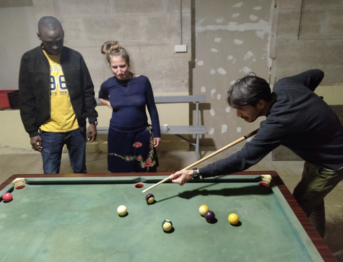 One of the Technoglob Collective takes a shot during a game of snooker while two others watch with anticipation.