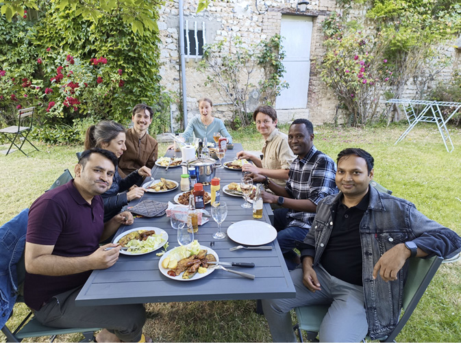 The Technoglob Collective eat dinner together in a garden of an old house with flowers growing up the walls.