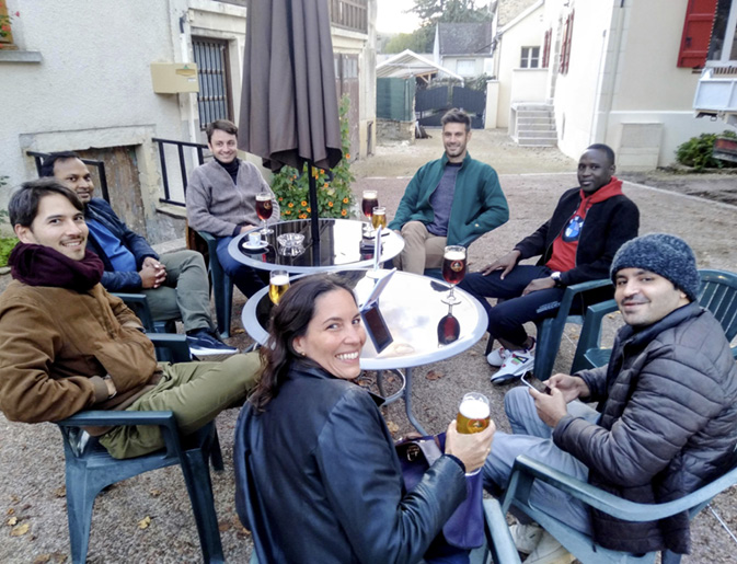 The Technoglob Collective sit outside a cafe around two tables enjoying a beer together, wrapped up in coats, hats and scarves.