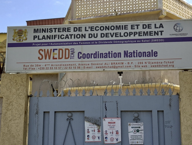 The outside of the SWEDD laboratory has yellow walls and a grey gate with barbed wire running across the top.